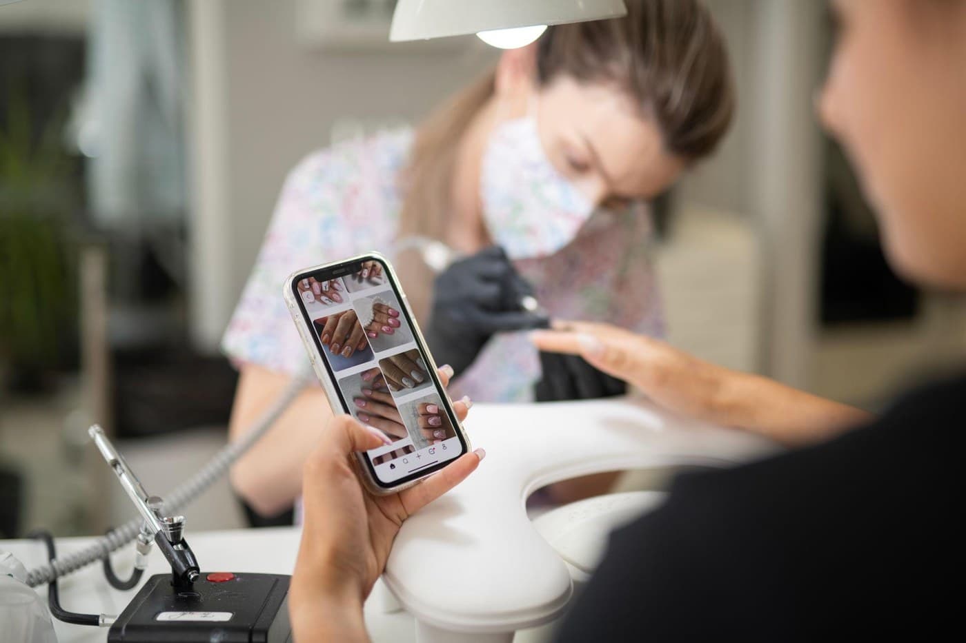 A client showing saved nail photos on her phone to a nail artist at the start of an appointment